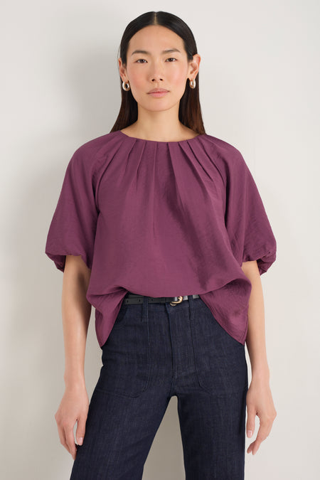Front view of model wearing a rich plum blouse with pleated neckline