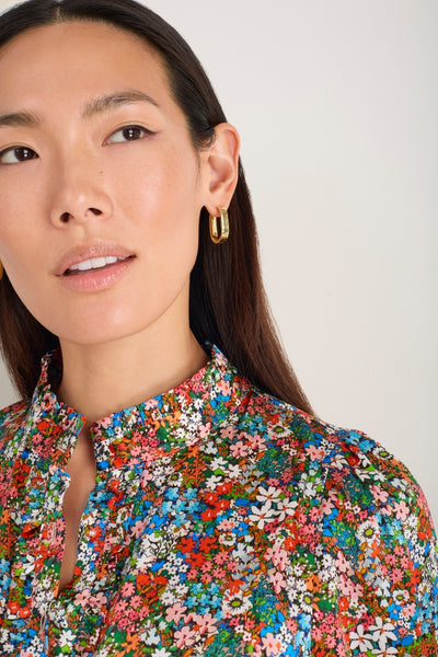 Detail of the Fabienne dress neckline, showing the ditsy floral pattern and gold earrings.
