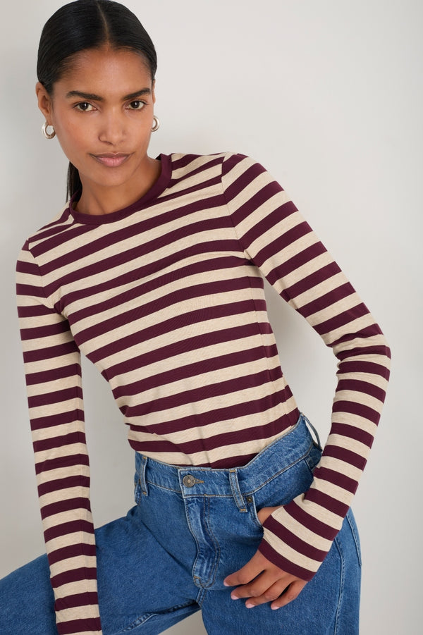 Model wearing a long-sleeved oat and deep fig striped jersey top with thumb holes.
