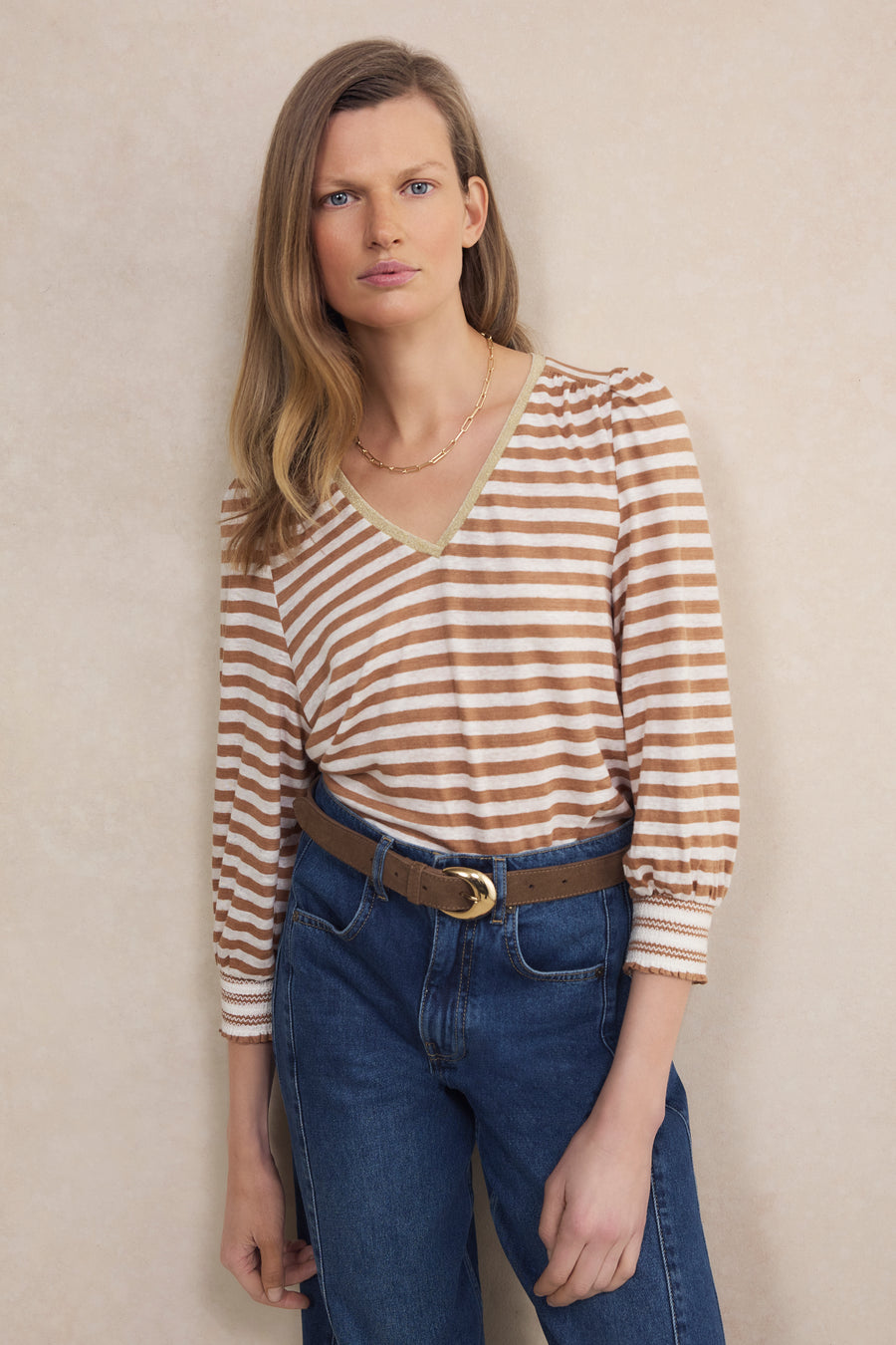 Woman wearing a striped shirt and blue jeans against a beige wall